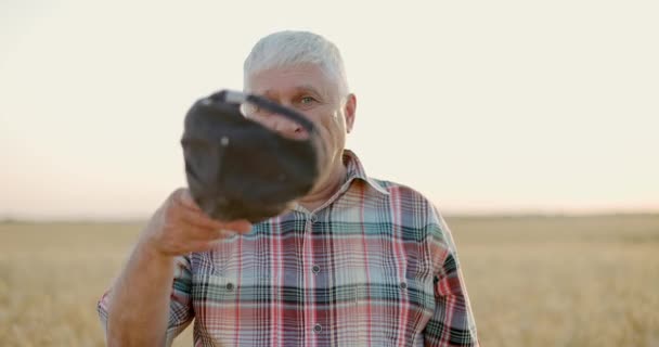 Веселий фермер у кепці, що стоїть серед стиглої пшениці перед заходом сонця. — стокове відео