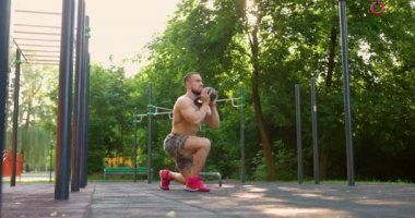 Kettlebell Spor Salonu 'nu kaldıran güçlü adam. Kaslı adam parkta kettlebell ile egzersiz yapıyor. Yavaş çekim