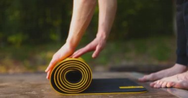 Yoga egzersizi yapan genç adam sarı yoga minderini parkta açıyor. Yakın plan. Açık havada. Sağlık konsepti. Yavaş çekim.