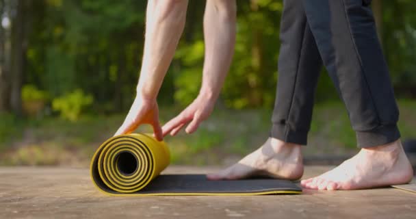 Preparación. Primer plano de hombre yog desenrollar lentamente alfombra de entrenamiento en el campo de deporte en el parque. Movimiento lento — Vídeos de Stock