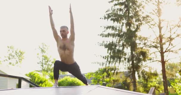 Hombre atlético haciendo ejercicios de pose de yoga y pilates en un bonito parque verde. Hombre haciendo yoga al aire libre. Concepto deporte, salud, fitness, bienestar, estilo de vida activo. Levanta las manos. — Vídeo de stock