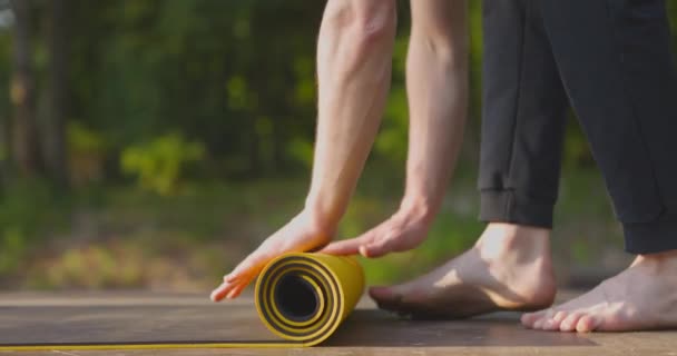 Primer plano de hombre yog lentamente rodar hasta alfombra de entrenamiento en el campo de deporte en el parque. Movimiento lento — Vídeos de Stock