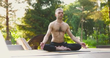 Yoga ve meditasyon yapan sportif bir adam. Yogi, yoga minderinin üzerinde lotus pozunda oturuyor.