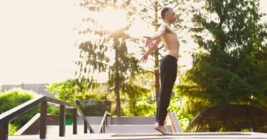Atletik adam yoga eğitimi alıyor. Adam yoga minderinde parmak ucunda dengede duruyor ve kollarını kaldırıyor.