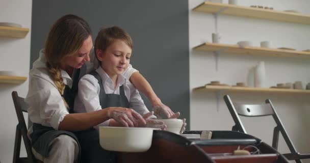 Jonge moeder en haar schattige zoontje werken samen op pottenbakkerswiel. Handgemaakte keramische werkplaats. Langzame beweging — Stockvideo