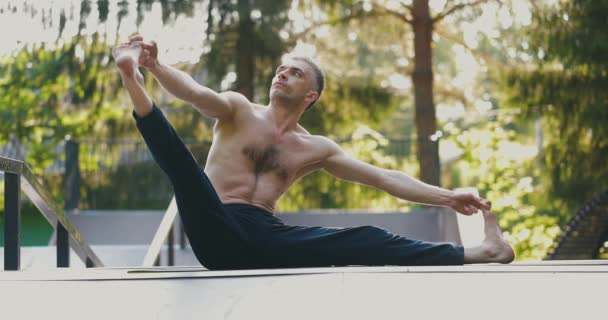 Atletische man stretching op yoga mat buiten.Yogi houdt benen met zijn handen en tilt een been omhoog — Stockvideo