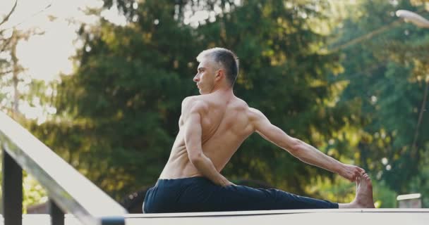 Чоловік займається розтягуванням під час практики йоги на самоті в міському парку. Спортсмен виконує скручування вправ — стокове відео