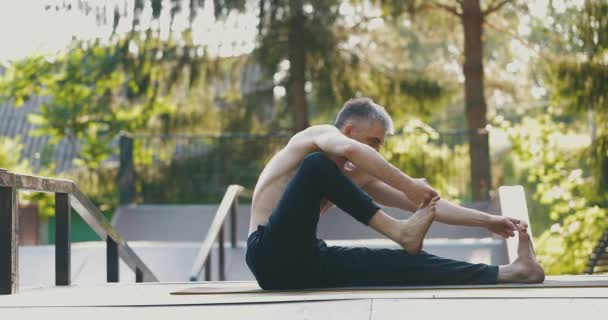 Чоловік розігріває тіло перед тренуванням йоги. Спортсмен сидить з прямими ногами, тримаючи пальці руками — стокове відео