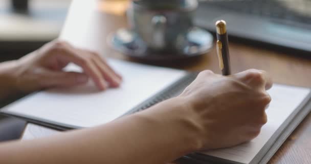 Primer plano de las manos de las mujeres jóvenes escribiendo notas personales en el cuaderno encuadernado en anillo sentado en la mesa de la cafetería — Vídeos de Stock