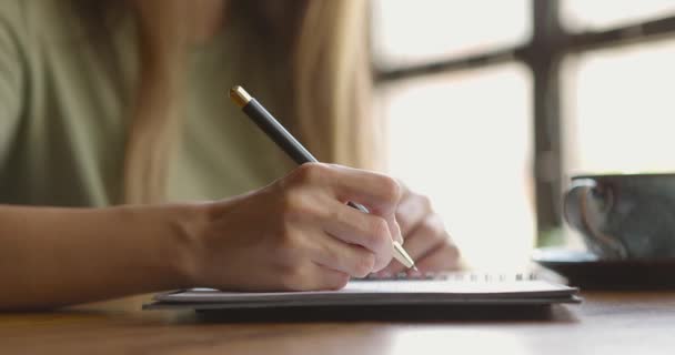 Mujeres manos escribiendo pensamientos en cuaderno. Mujer sentada en acogedora cafetería, tomando café, tomando notas — Vídeos de Stock
