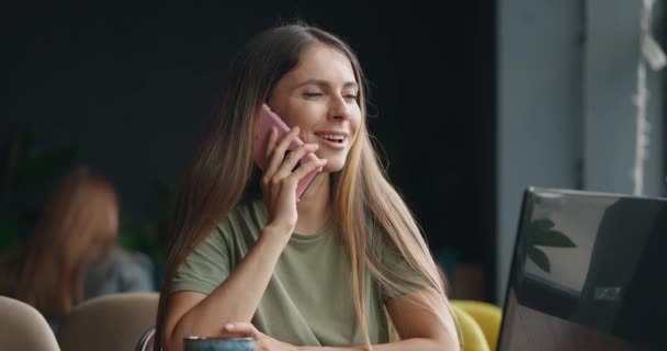 Улыбающаяся деловая женщина разговаривает по телефону и работает со своим ноутбуком в кофейне — стоковое видео