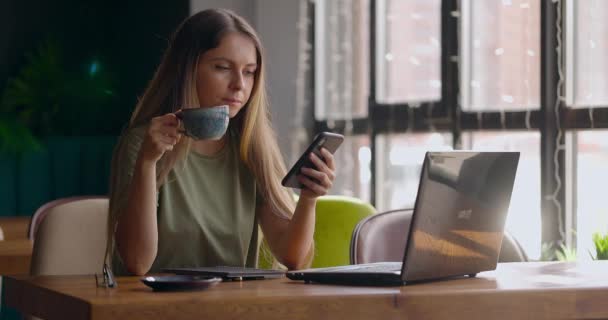 Hermosa mujer en acogedora cafetería tomando una taza de café y comprobando mensajes en el teléfono inteligente — Vídeos de Stock
