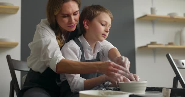 Glückliche junge Frau und niedlicher kleiner Junge, die in der Werkstatt auf einer Spinnmaschine Töpferwaren herstellen. Zeitlupe — Stockvideo