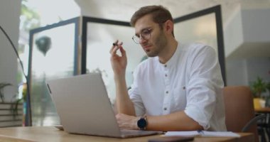 Modern kafede dizüstü bilgisayarla çalışan yakışıklı bir adam. İş adamı düşünüyor ve proje üzerinde çalışıyor.