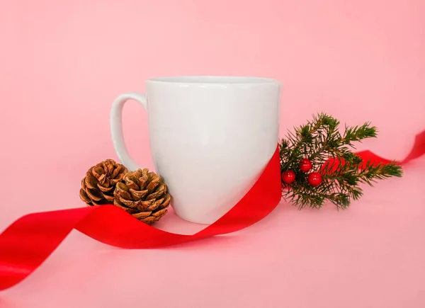 White mug and christmas decoration on a pink background.