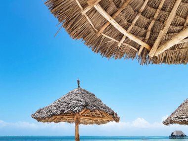 Sahilde mavi gökyüzüne karşı saman şemsiyesi, asgari konsept