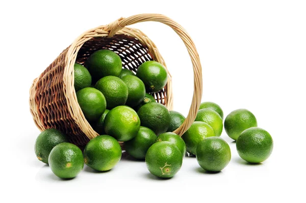 Pile of green limes and straw basket — Stock Photo, Image