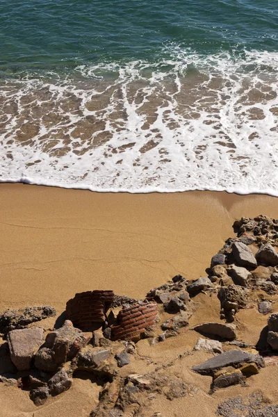 Onda quebrando em uma praia com rochas e ruínas — Fotografia de Stock