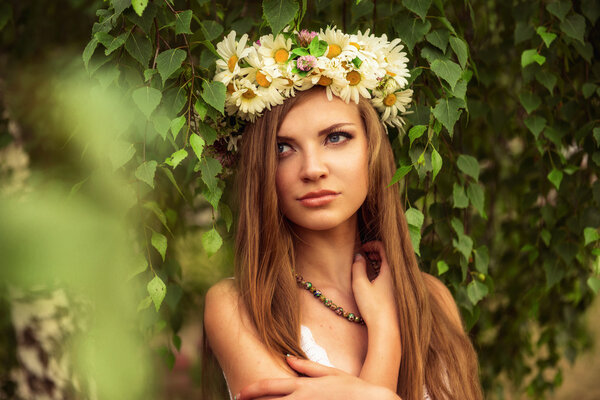 Young beautiful woman outdoor in a birchwood wearing wreth of daisy flowers