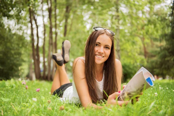 Eine junge brünette Frau, die mit ihrem Fuß im Gras liegt — Stockfoto