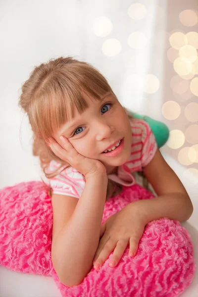 Cute little girl lying on a heart shaped pillow at home. Holiday — Stock Photo, Image