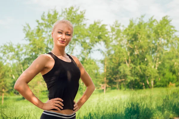 Young woman in sportswear standing outdoors in a park on sunny s — Stock Photo, Image