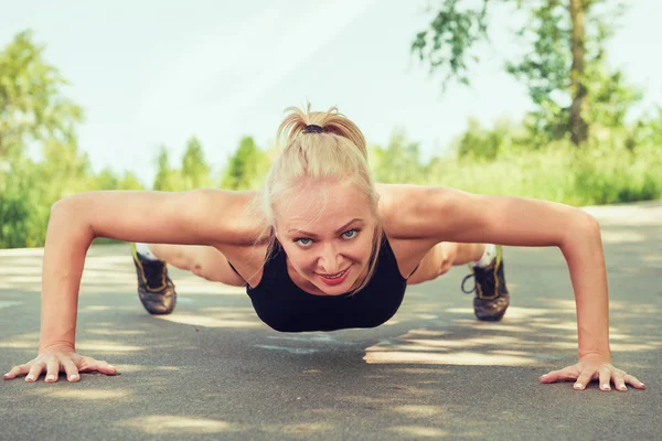 Young woman doing push ups outdoors in a park on sunny summer da — Stock Photo, Image