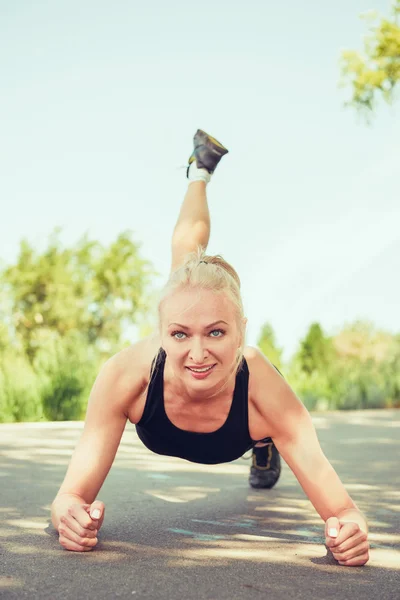 Young woman doing push ups outdoors in a park on sunny summer da — Stock fotografie