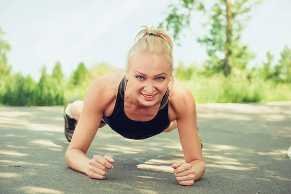 Young woman doing push ups outdoors in a park on sunny summer da Stok Fotoğraf