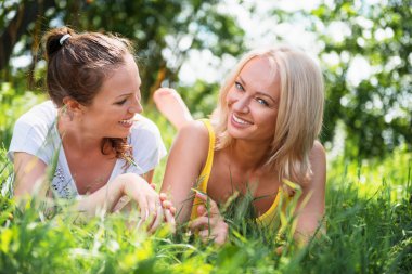 İki sevimli genç kadın yaz güneşli gün outd çimlere yatan