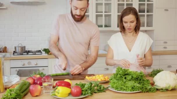 Giovane coppia che cucina insieme e parla in cucina tagliando verdure e ripieno di pollo per la cena a casa — Video Stock