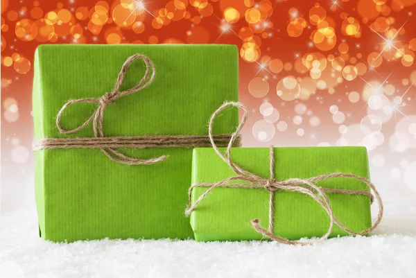 Dos regalos verdes en la nieve, efecto Bokeh rojo complementario —  Fotos de Stock