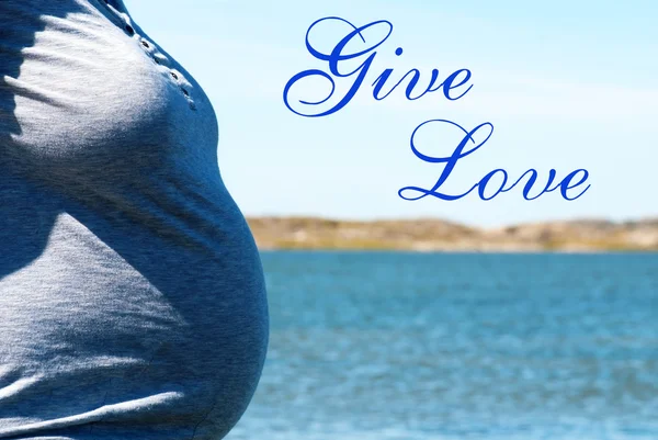 Mulher grávida em frente mar azul com texto Dê amor — Fotografia de Stock