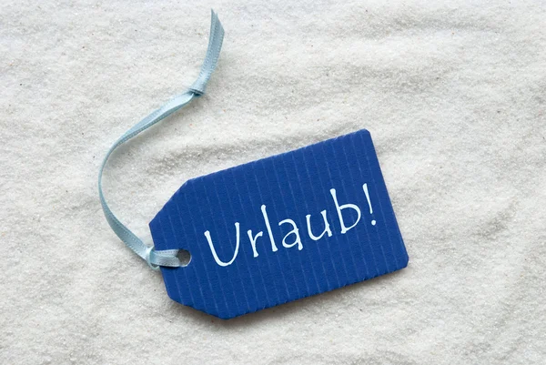 Urlaub anlamına gelir tatil mavi etiket üzerinde kum arka plan — Stok fotoğraf