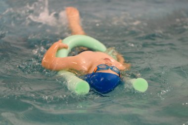 Yeni yürümeye başlayan çocuk havuzda yüzme eğitimi alıyor. Bir çocuk için yüzme eğitimi. Çocuk sporlarının gelişimi. Bebeğin sağlığını güçlendiriyor.