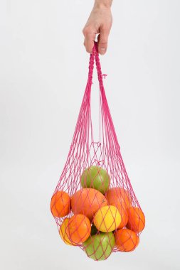 Beyaz arka planda bir kadının elinde meyve dolu bir torba.