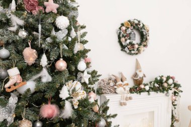 Beyaz klasik şöminenin arka planına karşı yumuşak pembe renklerde Noel süslemeleri ile süslenmiş Noel ağacı. Yeni yıl şenlikli oturma odasının ayrıntıları.