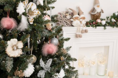 Beyaz klasik şöminenin arka planına karşı yumuşak pembe renklerde Noel süslemeleri ile süslenmiş Noel ağacı. Yeni yıl şenlikli oturma odasının ayrıntıları.