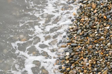 Dalgalar bir yaz günü çakıl taşı plajına çarpıyor. Üst Manzara. Deniz, sahil ve tatil temaları için arka plan.