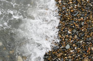 Dalgalar bir yaz günü çakıl taşı plajına çarpıyor. Üst Manzara. Deniz, sahil ve tatil temaları için arka plan.