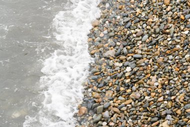 Dalgalar bir yaz günü çakıl taşı plajına çarpıyor. Üst Manzara. Deniz, sahil ve tatil temaları için arka plan.