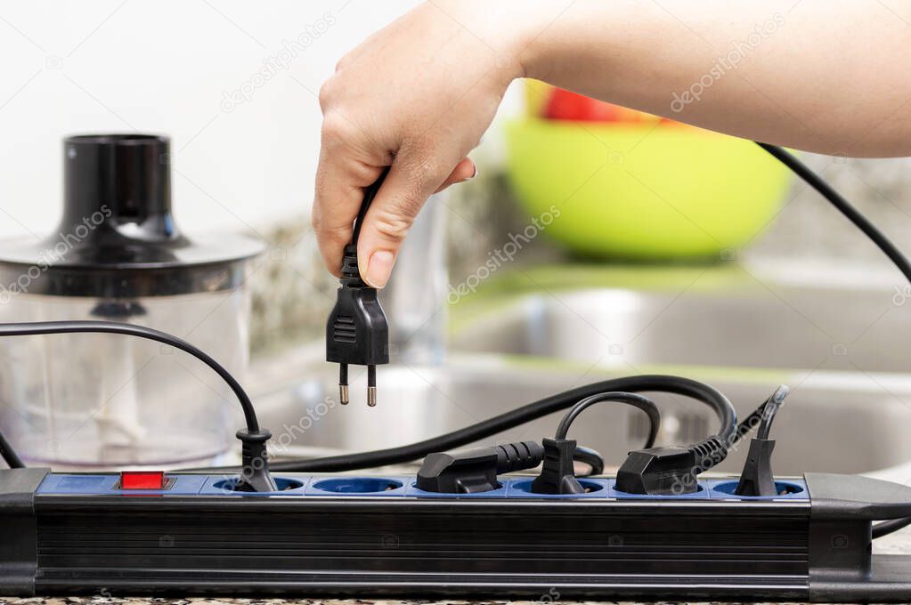 Close up of a woman hand plugging a plug in an electrical socket on a worktop at kitchen