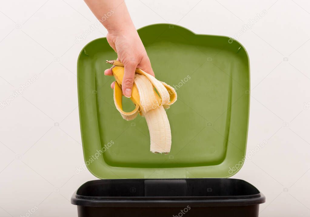 Close-up of a person throwing a half-finished banana into the bin.Concept of food waste that is in good condition