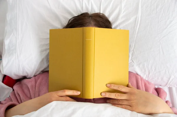 Woman sleep on bed with book cover his face, sleep late reading book prepare for exam.