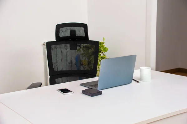 Cropped shot of laptop and a smart phone on a desk in an empty home office during the day.Focus on laptop
