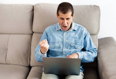 Evde dizüstü bilgisayarı üzerinde çalışan bir işadamı sinirli görünüyor.