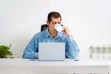 Bir iş adamını kahve içerken ve ofiste dizüstü bilgisayar kullanırken çekmişler.