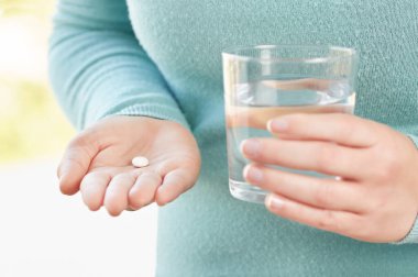 Tanımlanamayan genç bir kadının elinde bir hap ve bir bardak su.