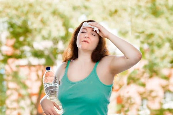 woman sweating suffering a heat stroke with a bottle of water at park