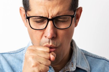 İzole edilmiş arka planda gözlük takan adam kendini kötü hissediyor ve soğuk algınlığı veya bronşitin belirtisi olarak öksürüyor. Sağlık hizmetleri kavramı.